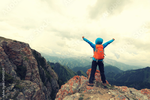 cheering successful woman backpacker open arms on mountain peak