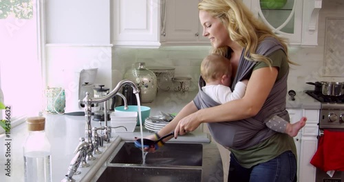 Busy Mother With Baby In Sling At Home 