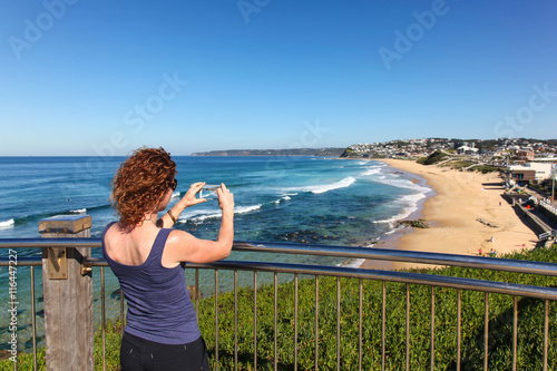 Woman takes a photo of Bar Beach - Newcastle Australia with her phone camera.