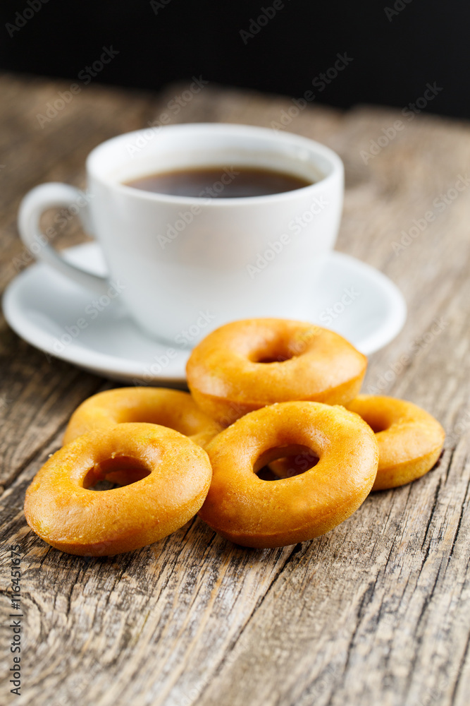 Orange vegetarian donuts with coffee for breakfast on wooden tab Orange vegetarian donuts with coffee for breakfast on wooden tab