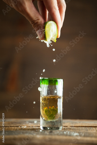 Squeezing lime into shot of tequila. Selective focus. Blurred background.