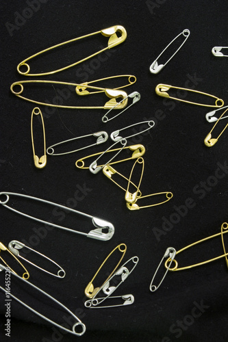 This is a photograph of Silver and Gold safety pins placed on a black piece of fabric