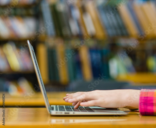 Hands typing on notebook in library