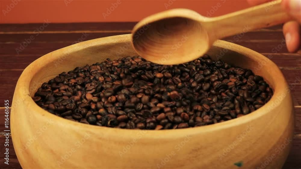 Coffee beans in a wooden plate stirring with a spoon on brown wooden table Coffee beans in a wooden plate stirring with a spoon on brown wooden table
