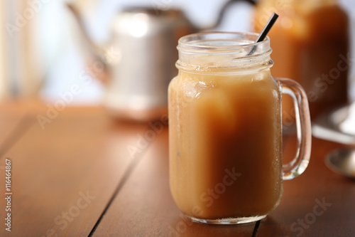 Iced coffee in glass jar with straw on brown wooden table