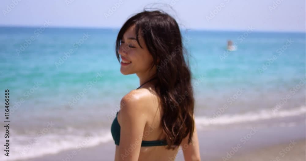 Smiling friendly beautiful woman with long dark hair standing on a tropical beach in a bikini with an ocean backdrop Smiling friendly beautiful woman with long dark hair standing on a tropical beach in a bikini with an ocean backdrop