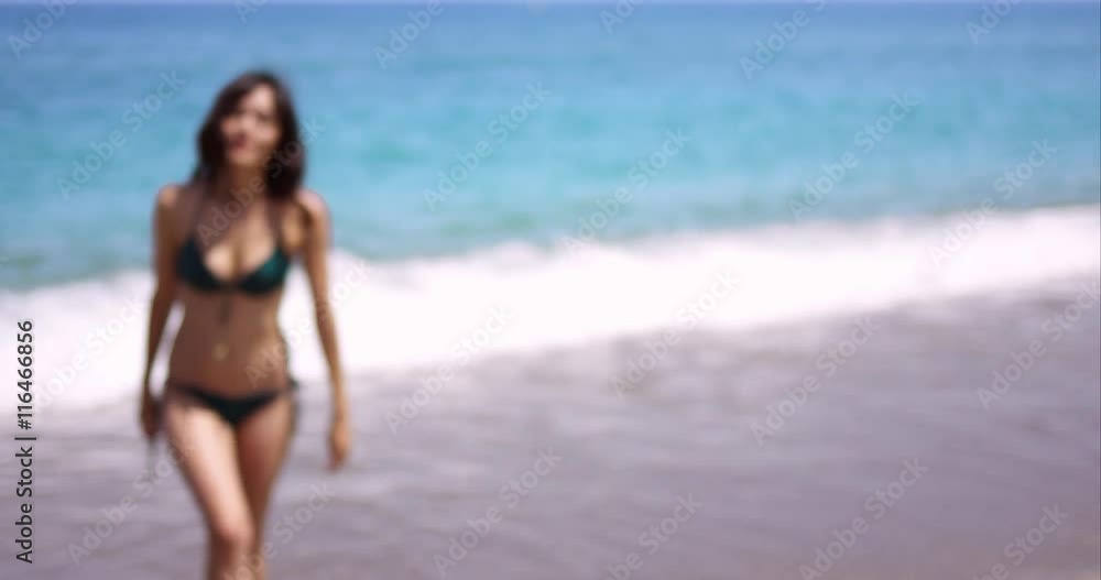 Pretty friendly young woman wearing a bikini standing with her back to the sea on a beach smiling at the camera Pretty friendly young woman wearing a bikini standing with her back to the sea on a beach smiling at the camera