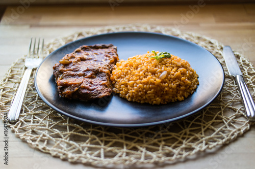 Steak with tomato sauce and bulgur rice in a black plate