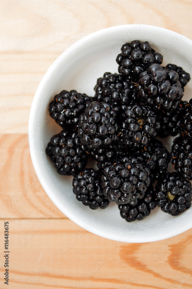 Blackberries in a white plate on a wooden board Blackberries in a white plate on a wooden board