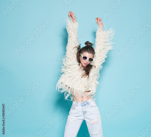 portrait of cheerful fashion hipster girl going crazy making funny face and dancing. Blue color background.