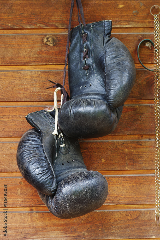 Old black boxing gloves hanging on wooden wall
