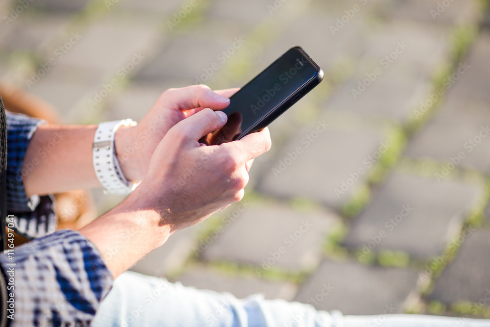 Closeup of male hands is holding cellphone outdoors on the street. Man using mobile smartphone.