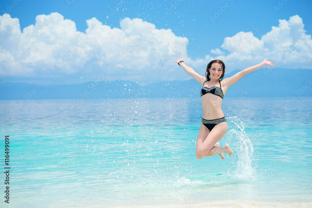 Young european woman is juming on the beach of tropical calm sea with white sand and blue sky Young european woman is juming on the beach of tropical calm sea with white sand and blue sky