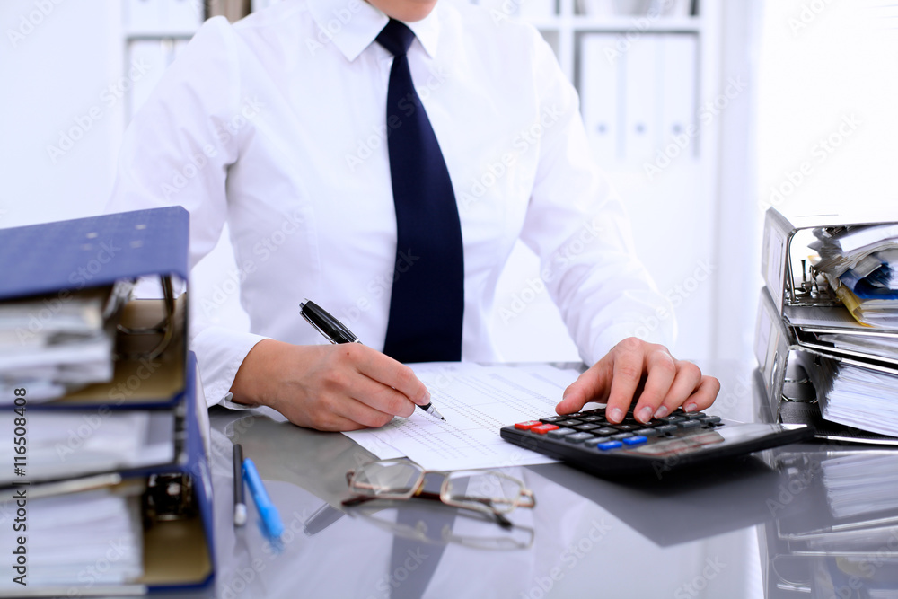 Bookkeeper or female financial inspector making report, calculating or checking balance. Internal Revenue Service checking financial document. Audit concept. Bookkeeper or female financial inspector making report, calculating or checking balance. Internal Revenue Service checking financial document. Audit concept.