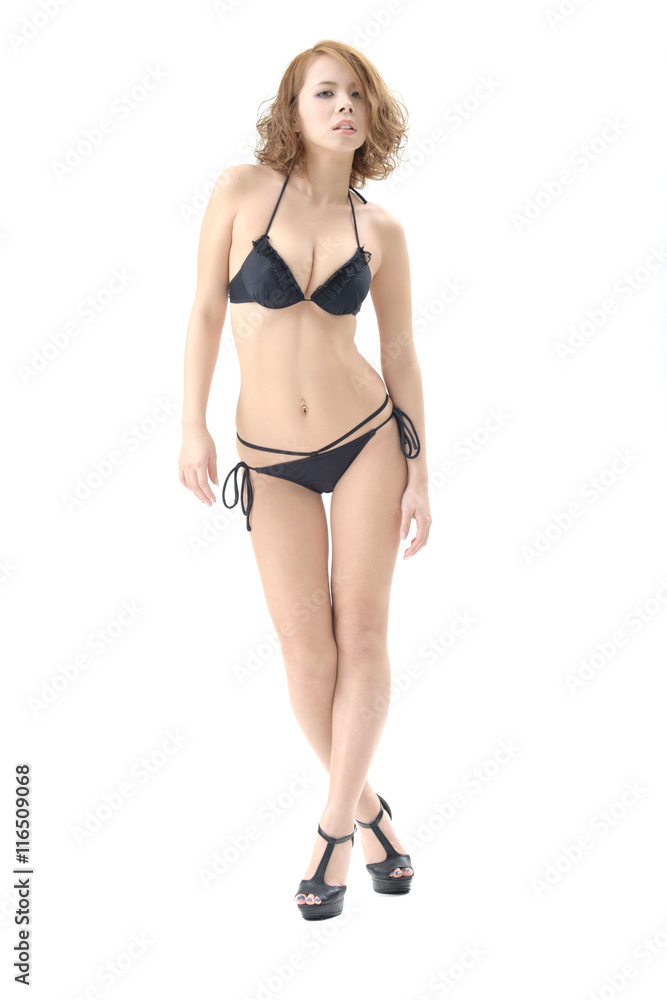 金髪の女性モデルが、黒いビキニの水着を着て立っています。この画像はスタジオで撮影されて物で、背景は白バックです。