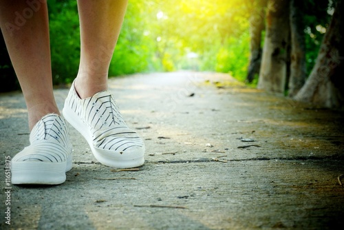 women legs and shoes walking on street in a parks , morning walk with green nature sunlight background, concept of journey travel or sport background