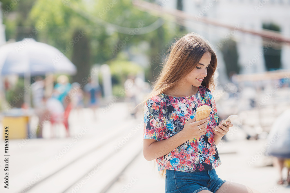 Summer portrait of beautiful woman with long straight brown hair,a nice smile,right hand holding an ice cream cone,reads the message on the mobile phone in summer Park