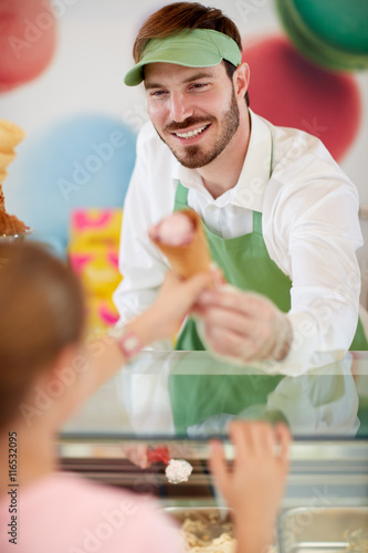Salesman in confectionery provides ice cream to girl