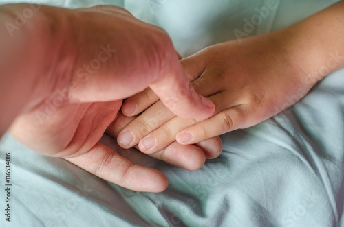 Close-up of a baby hand in father s hand on the blue bed.
