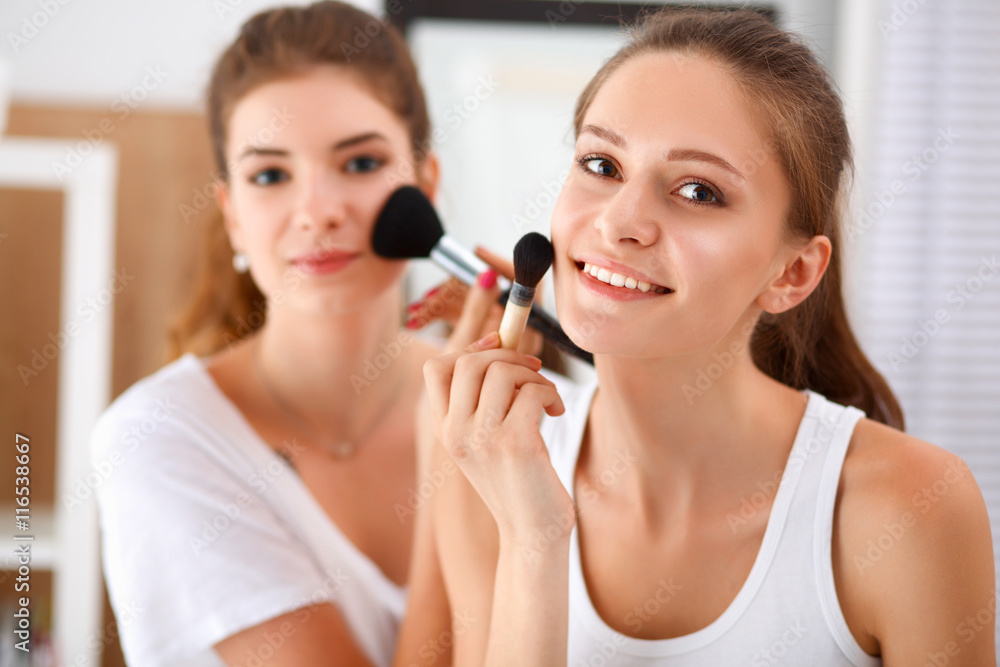 Beautiful girls looking in the mirror and applying cosmetic with a big brush Beautiful girls looking in the mirror and applying cosmetic with a big brush