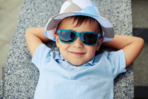 Close-up of small boy in sunglasses lying with hands under his h photo