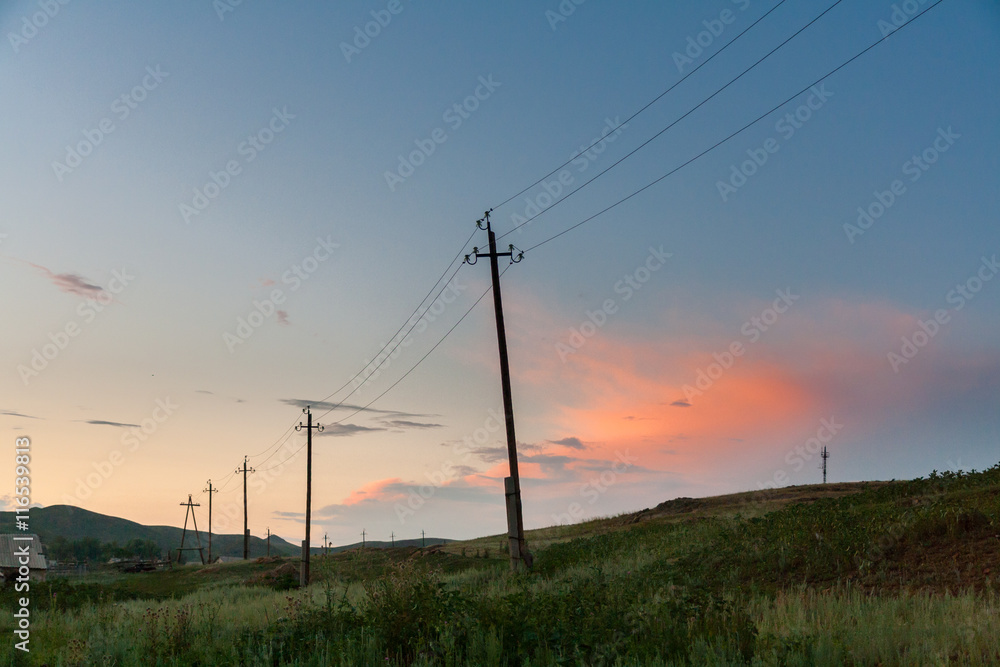 The old crooked poles of power lines on the steppe hills summer evening.