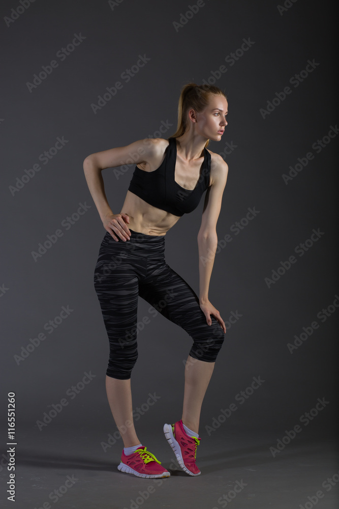 Body of slim female in activewear doing posin on gray low key, perfect blonde