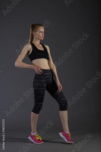 Body of slim female in activewear doing posin on gray low key, perfect blonde