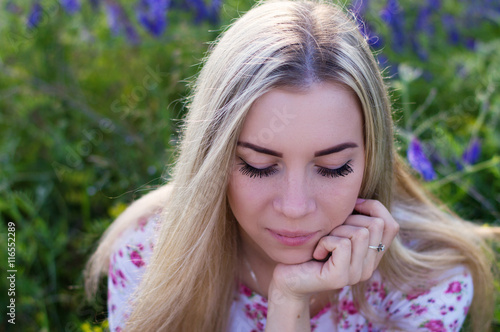 Portrait of a young blond female sitting near grass with eyes shut