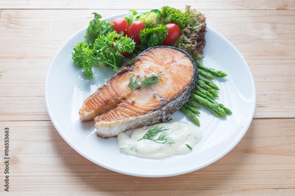 Fried salmon with vegetable on a round white plate on wooden bac Fried salmon with vegetable on a round white plate on wooden bac