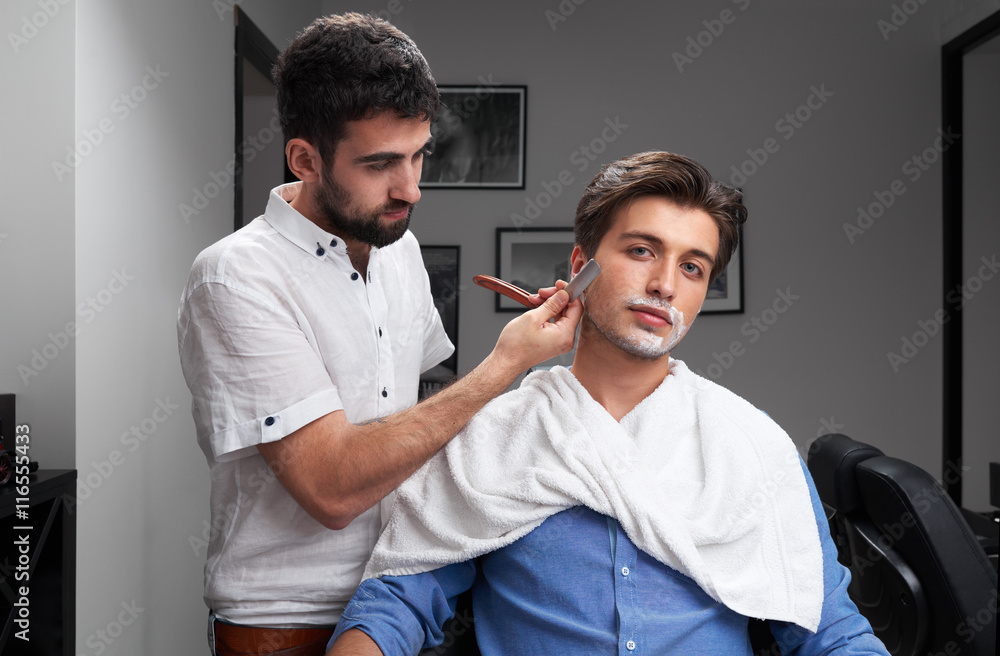 Obraz premium The barber is shaving the client's beard with razor