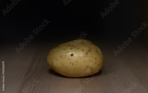 one yellow potato on wooden background   close up