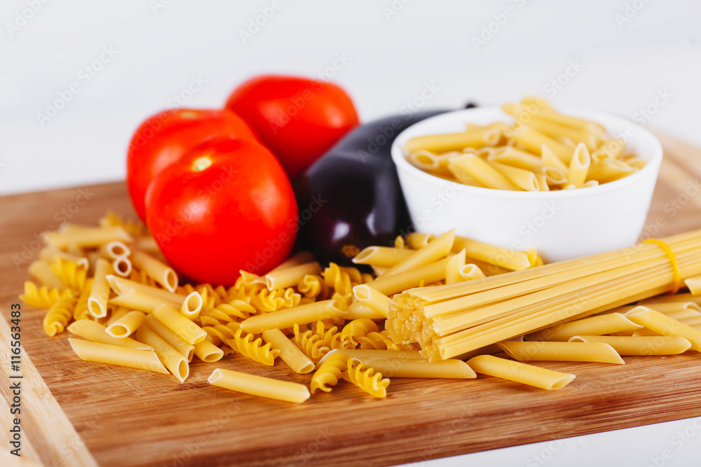 Different types of raw Italian pasta with tomatoes and other vegetables, top view background. Selected focus.