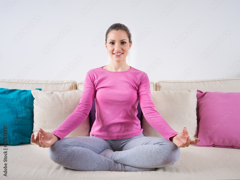 Beautiful young woman sitting on a sofa with her legs crossed and meditating. Beautiful young woman sitting on a sofa with her legs crossed and meditating.
