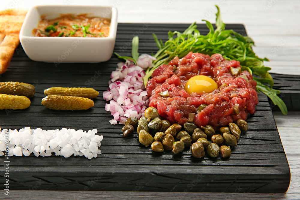 Steak tartar with chopped onion and herbs on wooden board