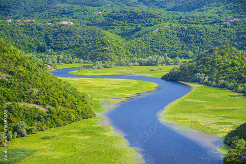 Meandering Rijeka Crnojevica river behind green mountains in Skadar Lake National Park, Montenegro, natural landscape background.