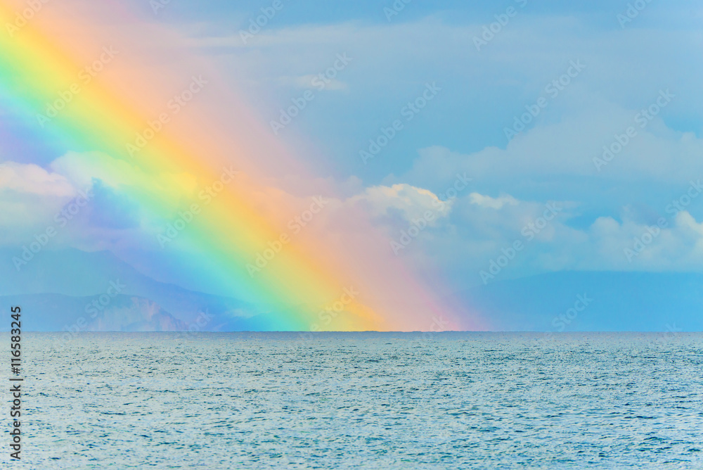 Beautiful seascape with big bright rainbow in clouds after the rain above the sea waves surface and mountains