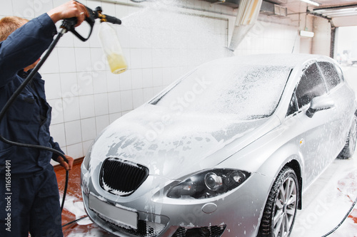 Serviceman in carwash washing car with hose. Handle automobile cleaning at special store, complex service