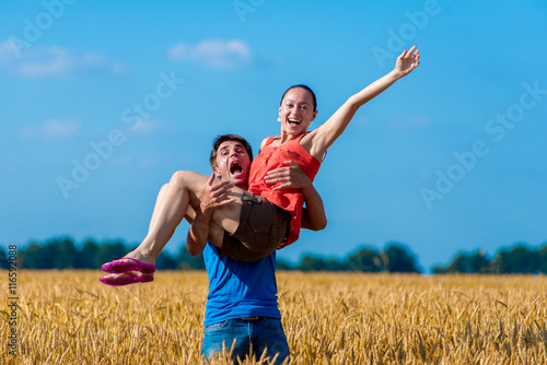 The guy carries the girl on sunset wheat field