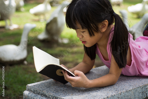 Little girl  lying on bench and read book in the park

