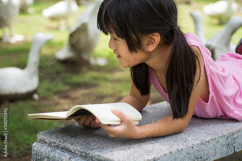 Little girl  lying on bench and read book in the park
