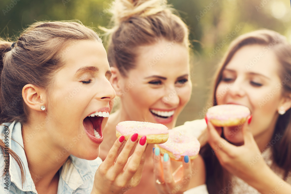Happy group of friends eating donuts outdoors