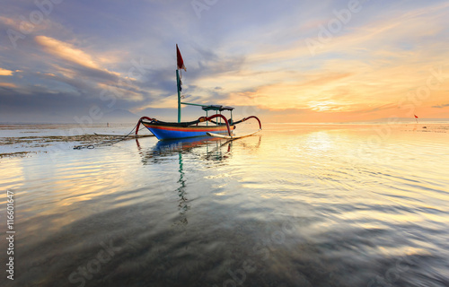 Traditional Balinese fishing boat Jukung during sunrise at Sanur beach in Bali, Indonesia photo