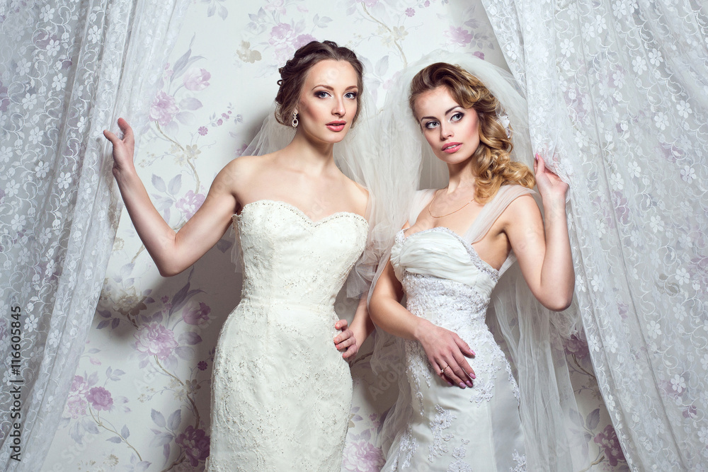 Two young beautiful European brides peep out through white curtains. Enigmatic look. Studio shot Two young beautiful European brides peep out through white curtains. Enigmatic look. Studio shot