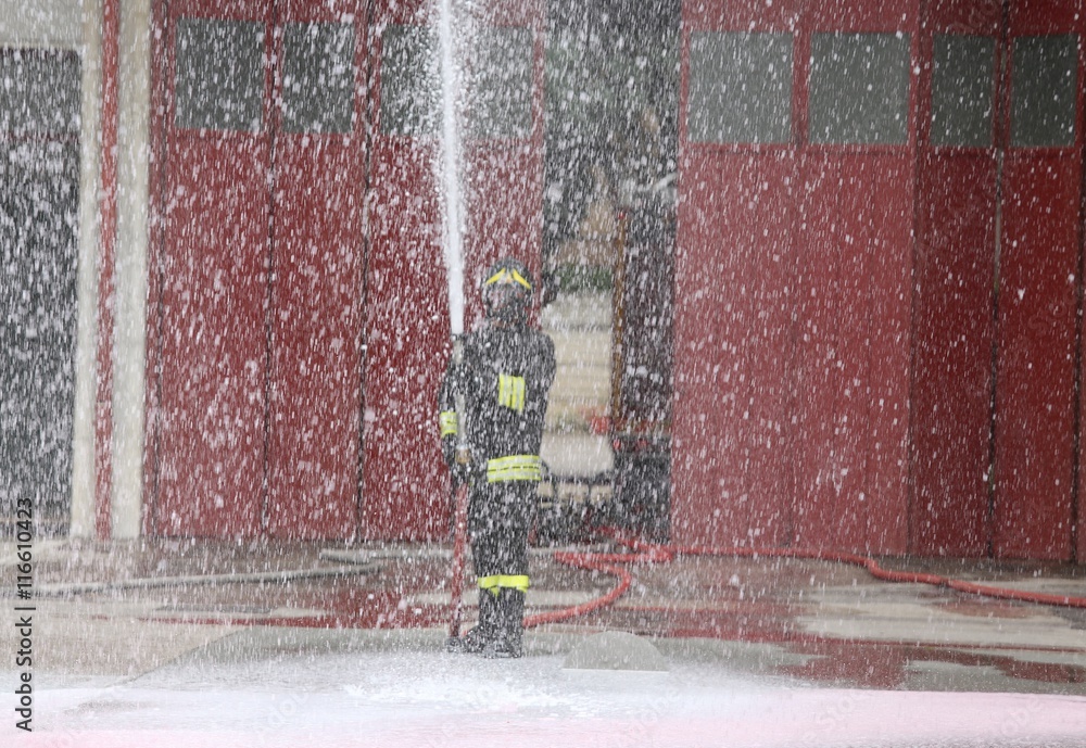 Naklejka premium brave fireman during the fire drill with the hose foam