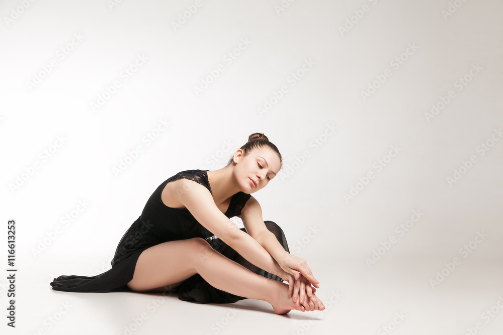 Young ballet dancer wearing black transparent dress sitting on floor