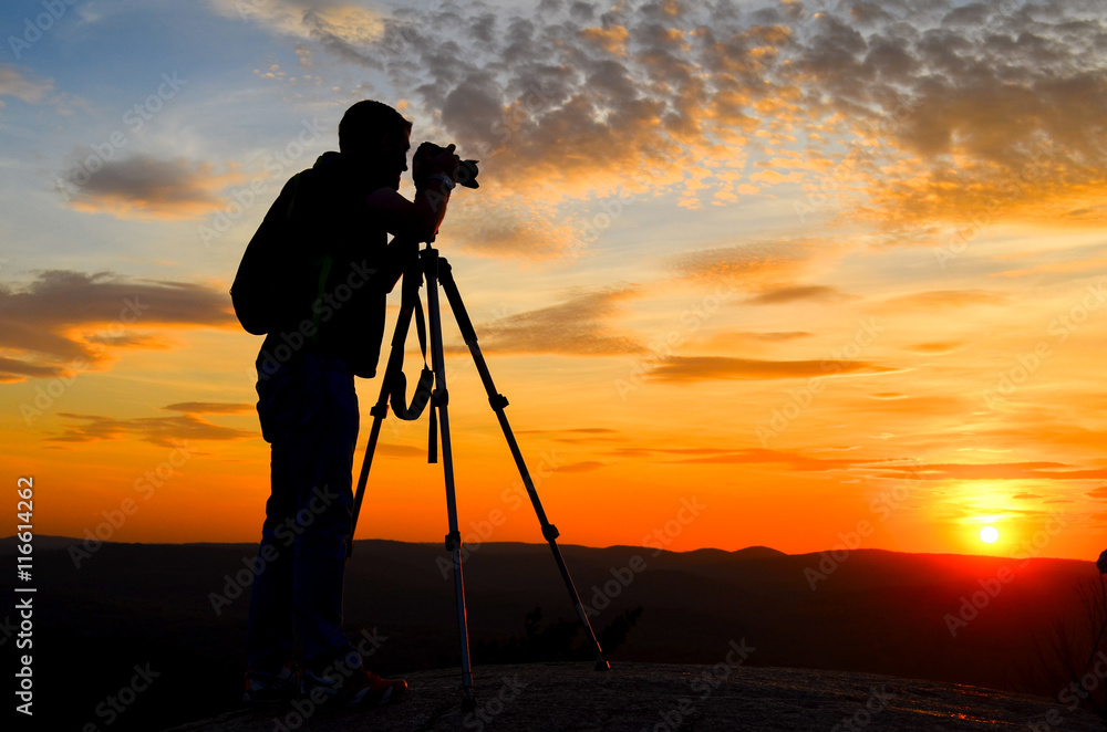 Silhouette of a nature photographer framing a shot, taking pictures at sunset in the mountains