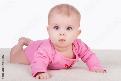 cute little baby girl with big blue eyes in pink bodysuit lying on a blanket and try crawling