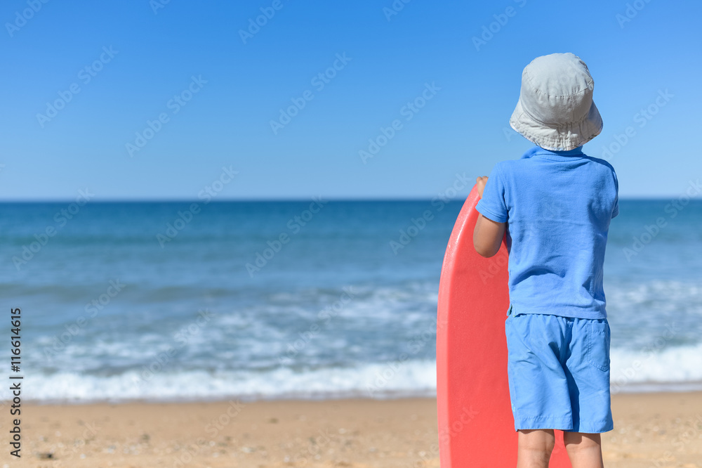 Back view of young man looking at the ocean on sunny beach, holding bodyboard