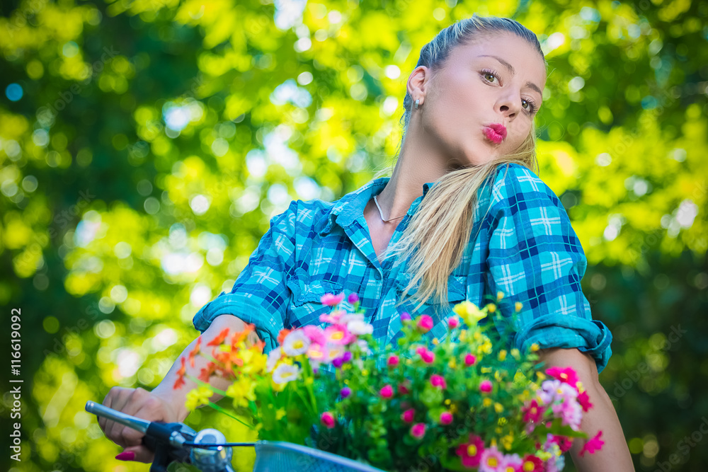 Portrait of pretty young female with pursed lips on bicycle with basket full of colorful flowers. Summer, nature, fashion and recreation concepts. Portrait of pretty young female with pursed lips on bicycle with basket full of colorful flowers. Summer, nature, fashion and recreation concepts.